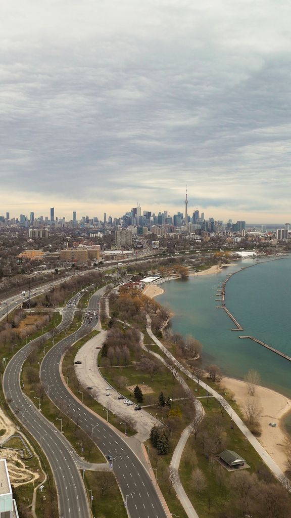 Drone shot of Toronto cityscape featuring Lake Ontario and winding highways under cloudy skies.