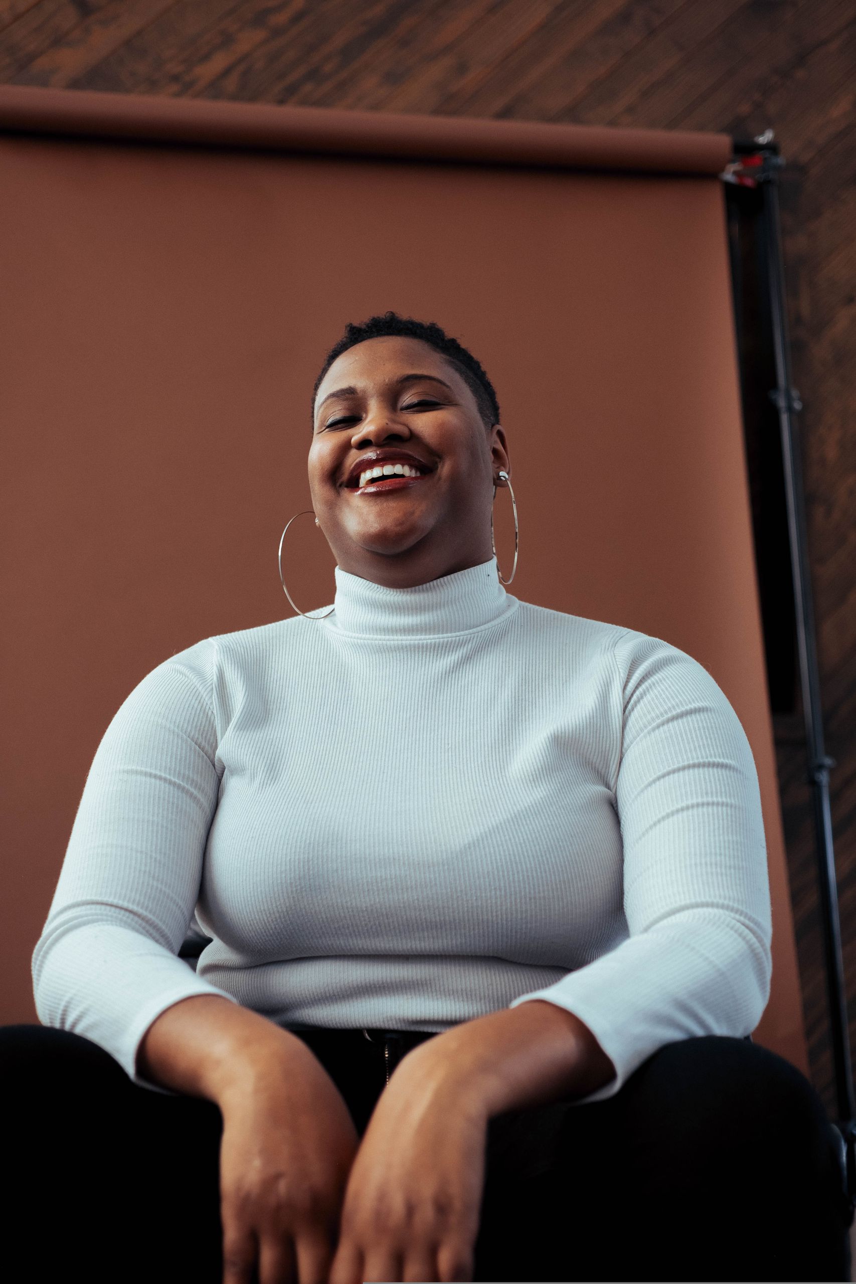 A joyful woman with a short hairstyle smiles confidently in a studio setting.